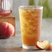 A glass of iced tea with a peach slice next to it.