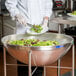 A chef in a white coat using a Vollrath heavy duty stainless steel mixing bowl to prepare a salad.