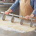 A person in an apron using an Ateco stainless steel multi-wheel pastry cutter to cut dough on a table.