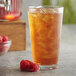 A glass of iced tea with raspberries and a bowl of raspberries on the side.