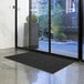 A black Lavex Needle Rib entrance mat placed in front of a glass door.
