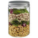A Solia clear plastic jar with salad and greens inside and a silver lid.