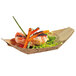 A Solia bamboo leaf boat dish filled with shrimp, carrots, and lettuce on a table.