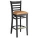 A black Lancaster Table & Seating wood bar stool with light brown vinyl seat.