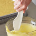 A hand using a white Linden Sweden bowl scraper to stir yellow cake batter in a bowl.