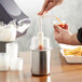 A person using a Steril-Sil stainless steel condiment dispenser kit to pour sauce into a container on a table.