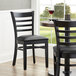 A Lancaster Table & Seating black wood ladder back chair with a black vinyl seat on a table in a restaurant dining area.