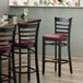 A Lancaster Table & Seating black wood ladder back bar stool with a burgundy vinyl seat detached.