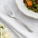 An Acopa stainless steel salad fork on a white plate with a salad.
