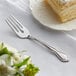 An Acopa stainless steel salad/dessert fork on a white plate with a piece of cake.