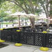 A black Grosfillex resin fence with yellow interlocking bases surrounding tables and chairs.