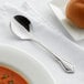 An Acopa stainless steel bouillon spoon on a napkin next to a plate of food.