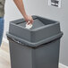 A person throwing a white tissue into a Lavex gray square trash can.