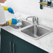 A person in blue gloves and yellow gloves cleaning a Waterloo stainless steel drop-in sink.