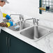 A person in gloves using a blue sponge to clean a Waterloo stainless steel drop-in sink in a professional kitchen.