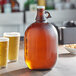 An Acopa amber glass growler with a cap and two glasses of beer.