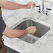A person washing hands in a Waterloo stainless steel undermount sink.