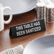 A black Cal-Mil table tent sign that says "This Table Has Been Sanitized" on a table.
