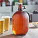An Acopa amber glass jug with a handle filled with beer next to two glasses of beer.