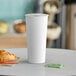 A close-up of a white Choice paper hot cup on a table with a croissant