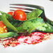 A plate with a fork and a leafy green salad with a tomato on it.