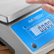 A person's hand using the AvaWeigh digital portion scale on a counter.