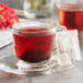 A glass cup of Wild Hibiscus Heart-Tee Hibiscus Herbal Tea with a tea bag on a saucer.