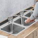 A person washing dishes in a Waterloo stainless steel drop-in sink with three compartments.