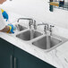 A gloved hand cleaning a Waterloo stainless steel drop-in sink.