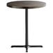 A round Lancaster Table & Seating bar height table with a wooden top and black cast iron base plate.