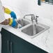 A person wearing blue rubber gloves washing a glass in a Waterloo two compartment sink.