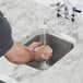 A person washing their hands in a stainless steel Waterloo sink under a running water.