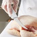 A person wearing a white glove uses a Choice curved boning knife to cut chicken.