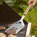 A person using an Outset stainless steel turner to cook burgers on a grill.