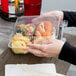 A hand holding a Durable Packaging clear plastic container with three compartments filled with food.