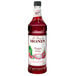 A close up of a Monin Premium Dragon Fruit flavoring syrup bottle full of red liquid.