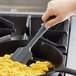 A hand holding a Tablecraft gray silicone spatula stirring scrambled eggs in a pan.