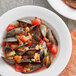 A white plate with a bowl of soup with mussels and tomatoes.