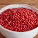 A bowl of Regal pink peppercorns on a wooden table.