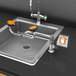 A Guardian Equipment left hand deck mounted eye and face wash station with a faucet and orange handle over a sink.