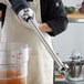 A person in a white apron using an AvaMix heavy-duty blending shaft to blend a brown drink.