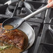 A Tablecraft stainless steel spoon with black silicone head pouring sauce on a meat dish.