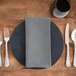 A black and white Milan birdseye cloth napkin on a plate with silverware on a wooden table.