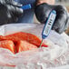 A person in gloves holding a blue AvaTemp digital pocket probe thermometer to a bag of fish.