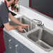 A man washing dishes in a Regency stainless steel drop-in sink with a faucet.