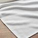 A white Milan birdseye banded cloth napkin on a wood surface.