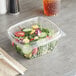 A salad in a Choice clear plastic deli container with a domed lid on a table.