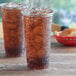 Two Choice clear plastic cups of iced tea on a table.