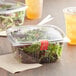 Choice 64 oz. clear plastic deli containers filled with salad on a table.