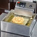 A deep fryer with a Carnival King stainless steel funnel cake mold ring in it.